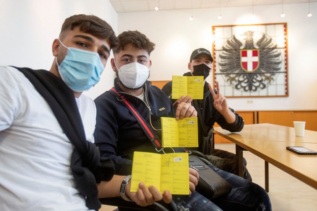 Ezek a fiúk már mehetnek bulizni, de az orvosi maszk már nem lesz elegendő a buszon: frissen oltott osztrák fiatalok mutatják védettségi igazolványukat a kamerának. Fotó: ALEX HALADA / AFP