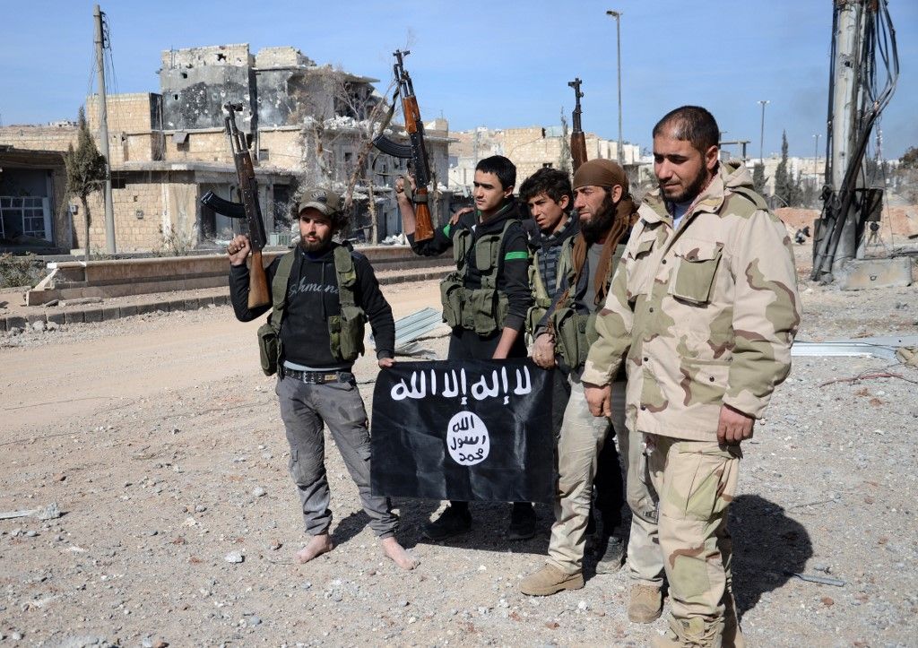 Iraki harcosok pózolnak egy legyőzött Iszlám Állam-csapat zászlójával. Fotó: NAZEER AL-KHATIB / AFP