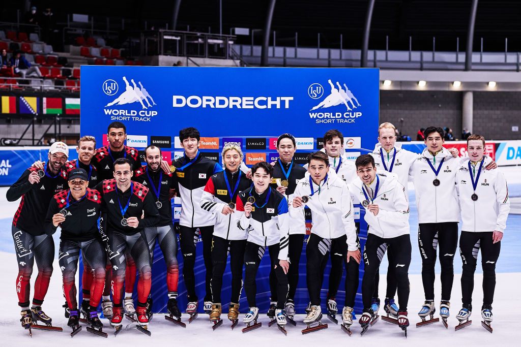 Az 5000 méteres férfiváltó versenyének eredményhirdetésén balra az ezüstérmes kanadai csapat, középen az aranyérmes dél-koreai együttes, jobbra a bronzérmes magyar alakulat a rövid pályás gyorskorcsolyázók dordrechti világkupaversenyén 2021. november 28-án. International Skating Union (Nemzetközi Korcsolyázószövetség)