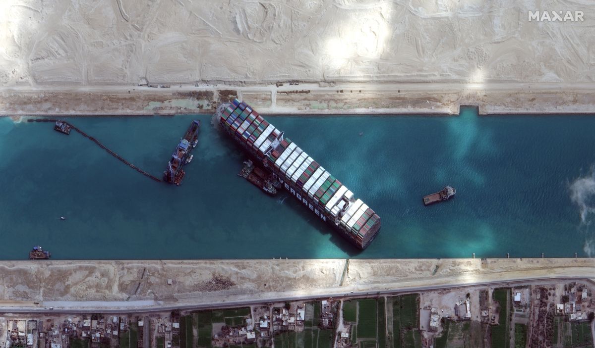 Munkagépekkel és vontatóhajókkal próbálják kiszabadítani a keresztbe fordult és beszorult Ever Given nevű konténerszállítót a Szuezi-csatornában 2021. március 28-án. (MTI/EPA/Maxar Technologies)