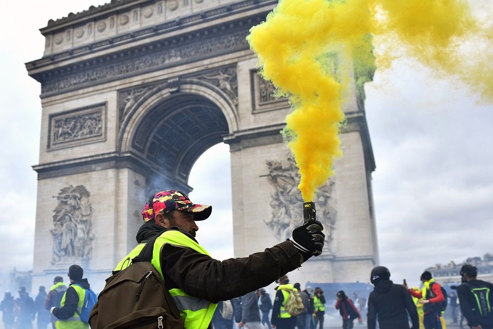 A francia kormány szociális és adópolitikája ellen tiltakozó sárgamellényesek egyike füstfáklyával demonstrál a párizsi Diadalívnél 2019. március 16-án, a tizennyolcadik egymást követő hétvégi tüntetésen. Az üzemanyagadó emelése ellen 2018. november 17-én kezdődött sárgamellényes mozgalom azóta több szociális jellegű követelést fogalmazott meg és Emmanuel Macron államfő távozását követeli. MTI/EPA/Julien De Rosa