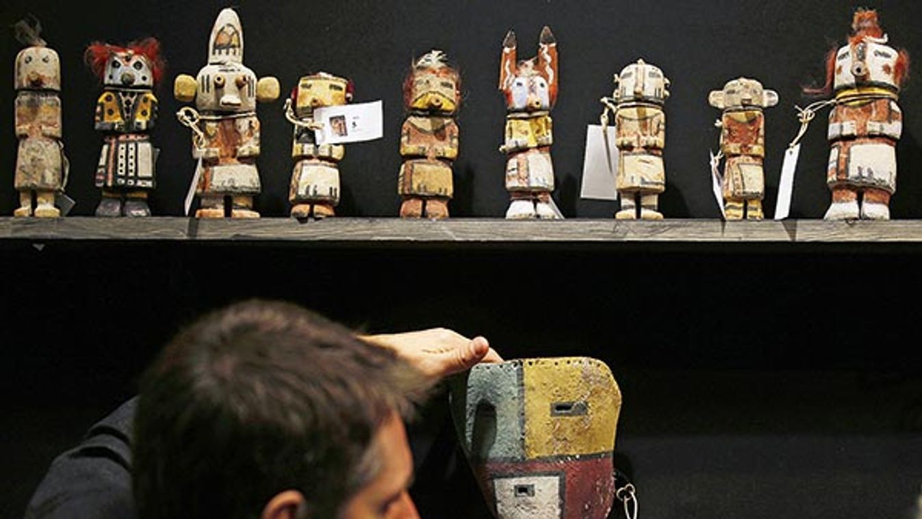 An expert hangs a rare antique Tuma Uyim mask below Kachina dolls made by the Native American Hopi and Zuni tribes displayed at the Drouot auction house in Paris before auction