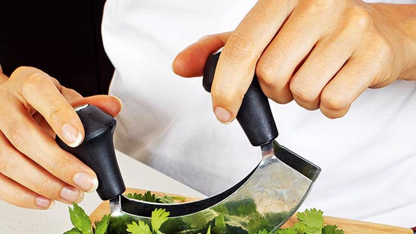 WOMAN IN KITCHEN CHOPPING CORIANDER WITH HACHOIR