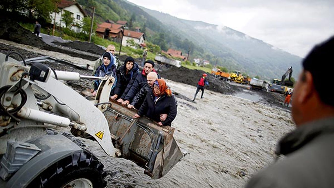 People are carried by a front loader as they evacuate from their flooded houses in Topcic Polje