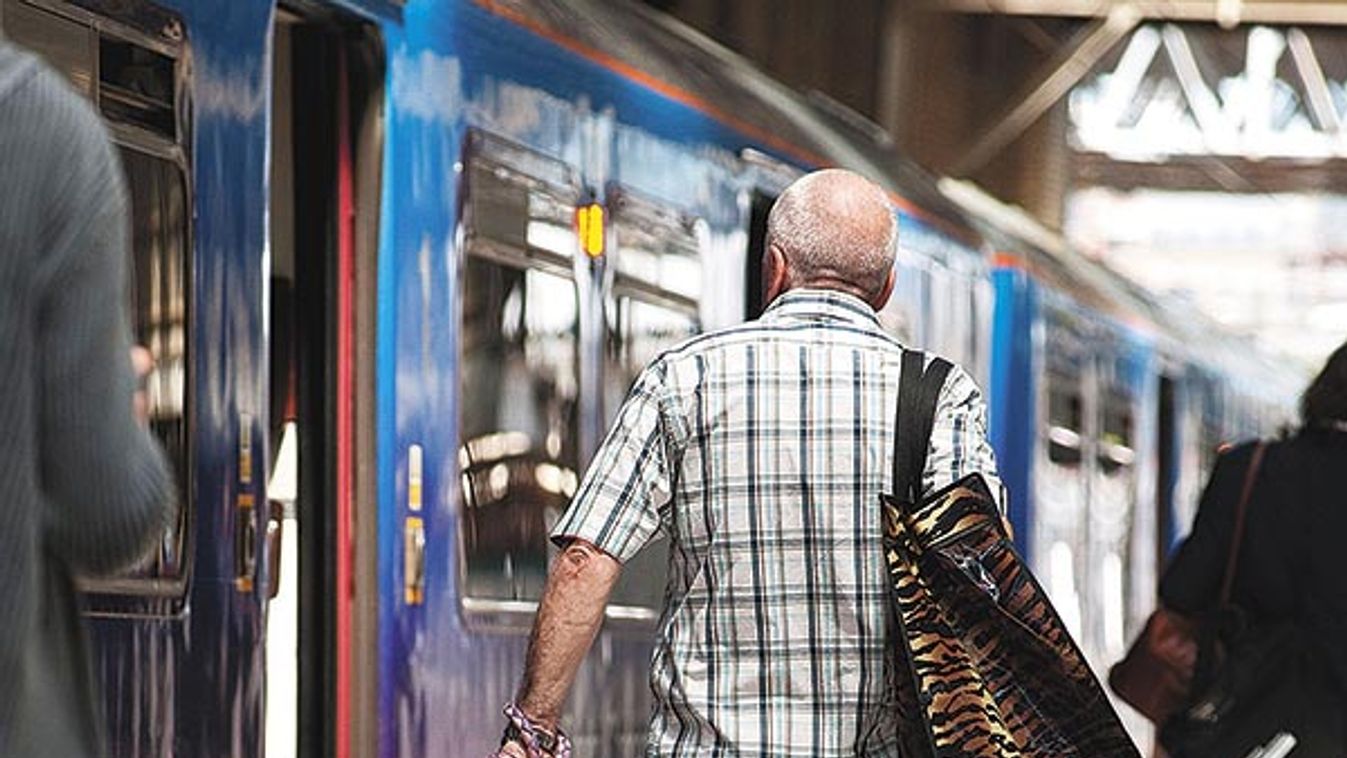 Rear view of a man and his dog walking along a platform at a railway station in England.