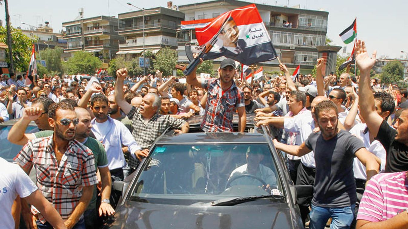 Mourners gather around a car carrying the coffin of the late Syrian Defense Minister Daoud Rajha during his funeral in Damascus