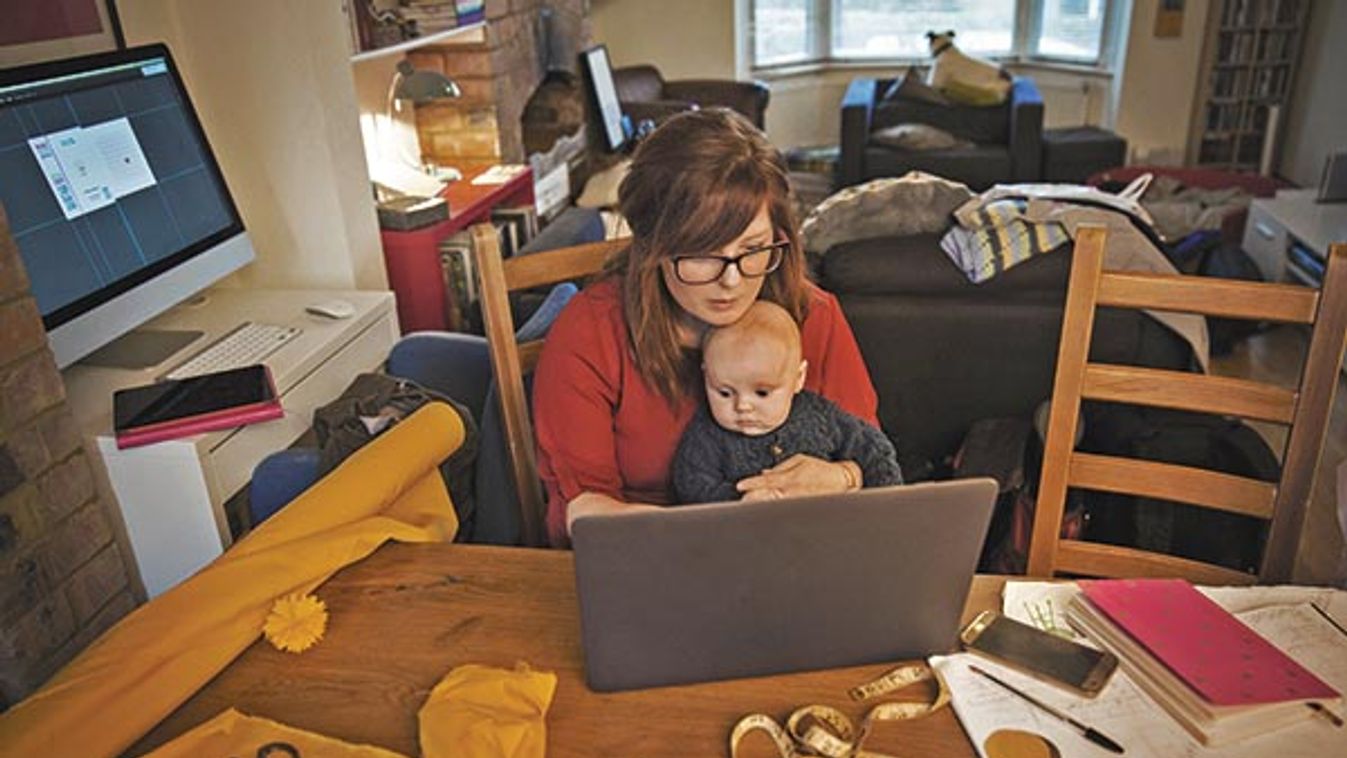 A woman seated with her baby on her lap, multitasking and using a laptop.
