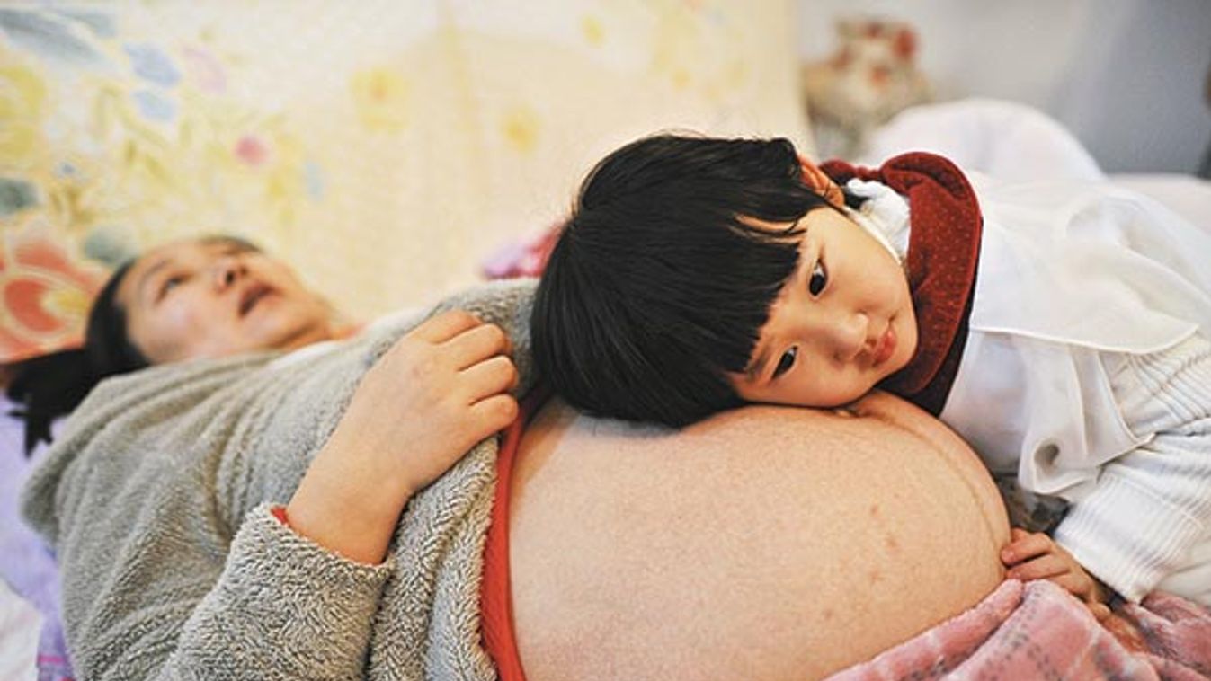 Li Yan, pregnant with her second child, lies on a bed as her daughter places her head on her mother's stomach in Hefei, Anhui province