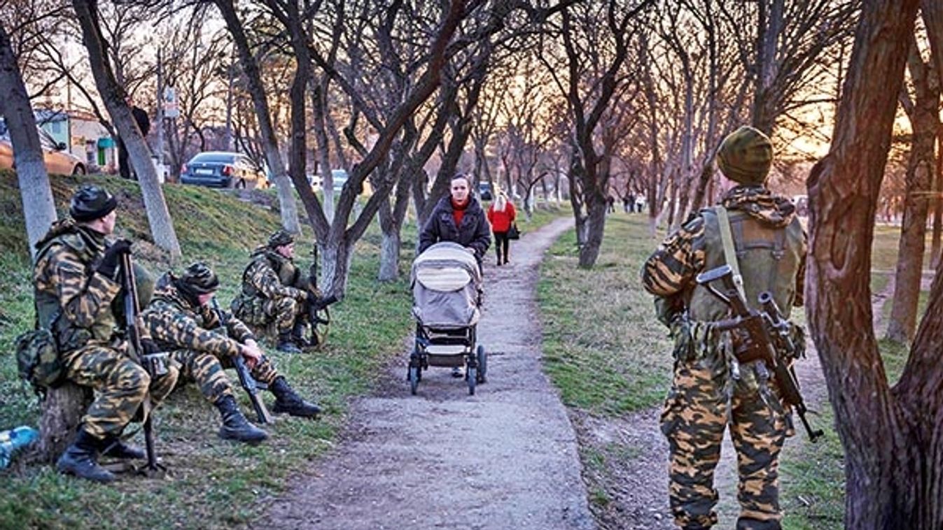 A woman pushes a stroller past Russian soldiers who have surrounded the Ukrainian military base in the village of Bakhchisarai, Ukraine.