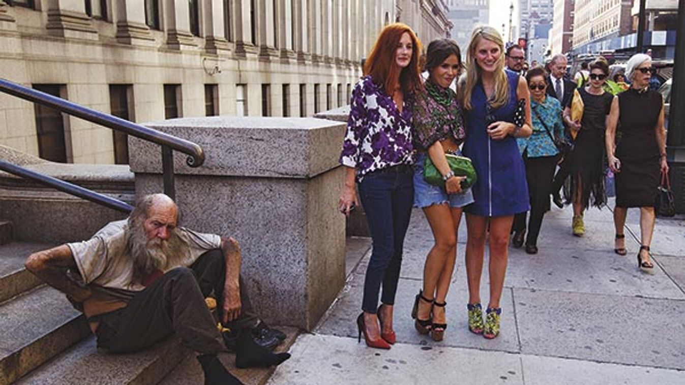 Fashionistas pose for photographs in front of a homeless man outside Moynihan Station following a showing of the Rag & Bone Spring/Summer 2013 collection during New York Fashion Week