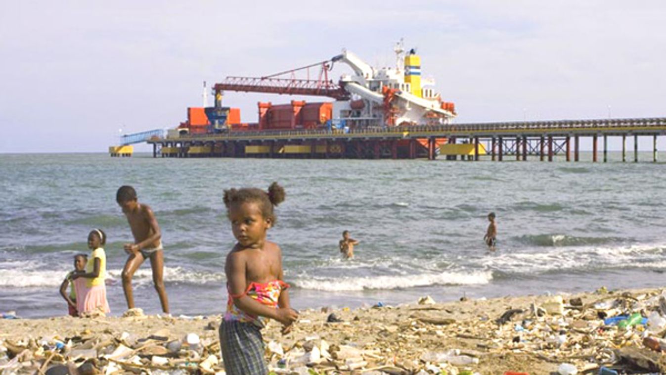 A girl stands on garbage while residents spend a day on the beach next to the main port in Haina