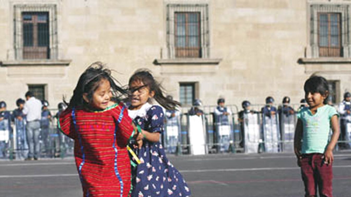 Indigenous girls play as police stand guard during a march marking the anniversary of a student massacre in Mexico City