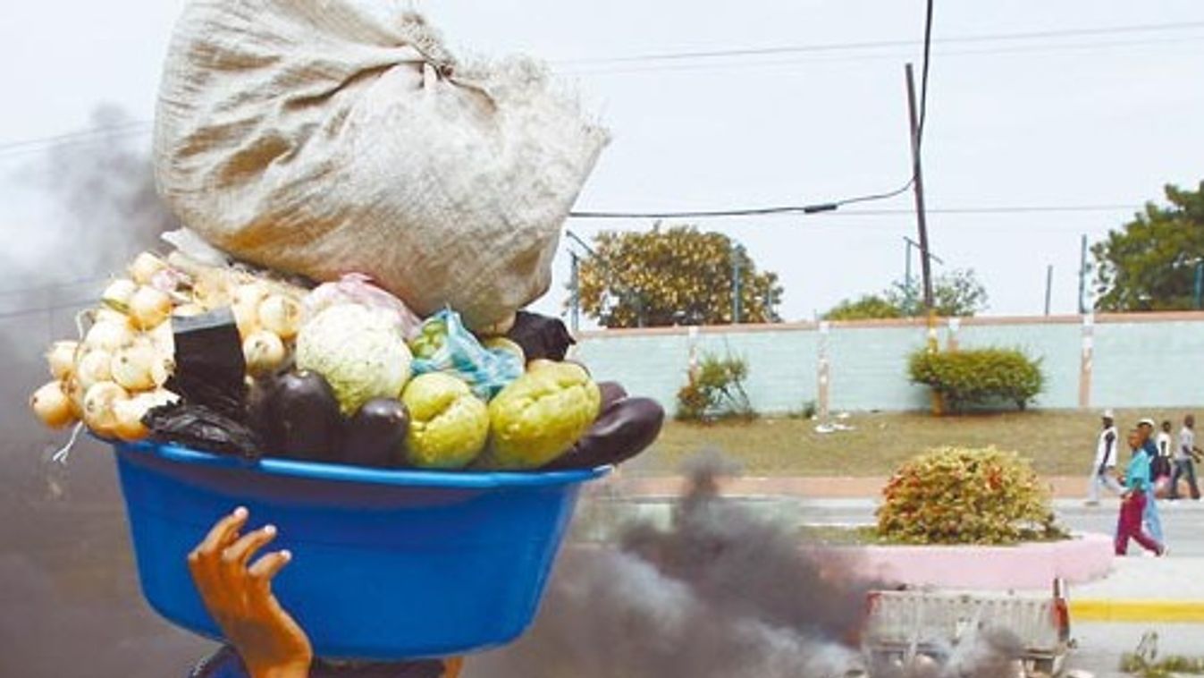 a Haitian woman walks while holding food as she crosses a barricade in Port-au-Prince