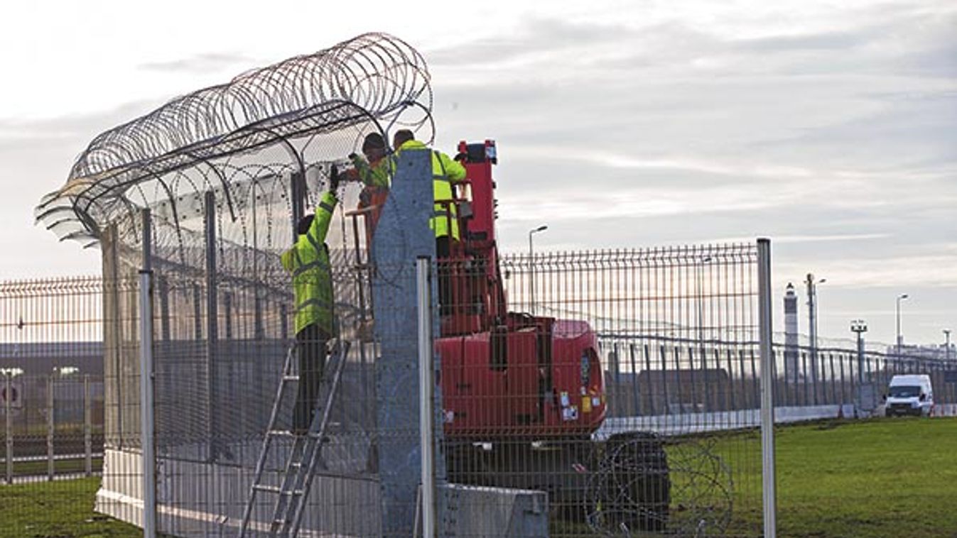 Workers build a fence to stop migrants from reaching the ferry harbour in Calais