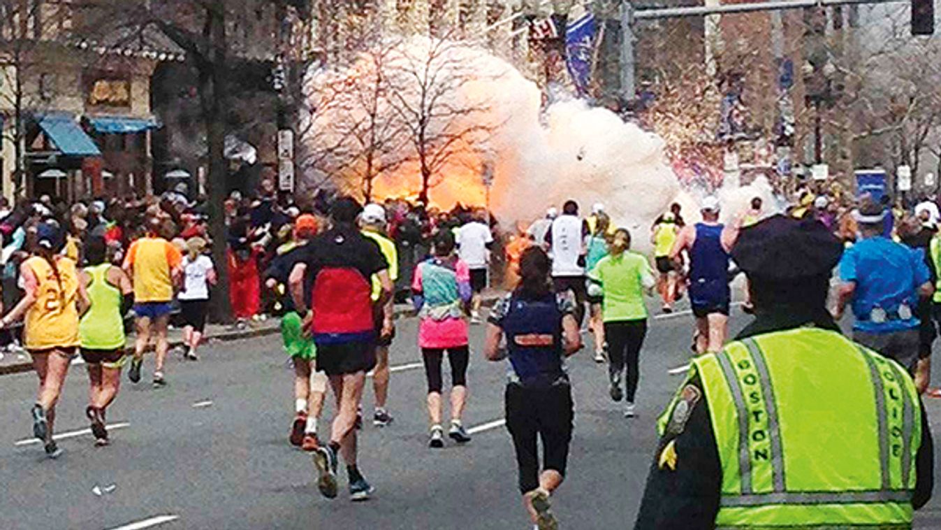 Runners continue to run towards the finish line as an explosion erupts at the finish line of the Boston Marathon