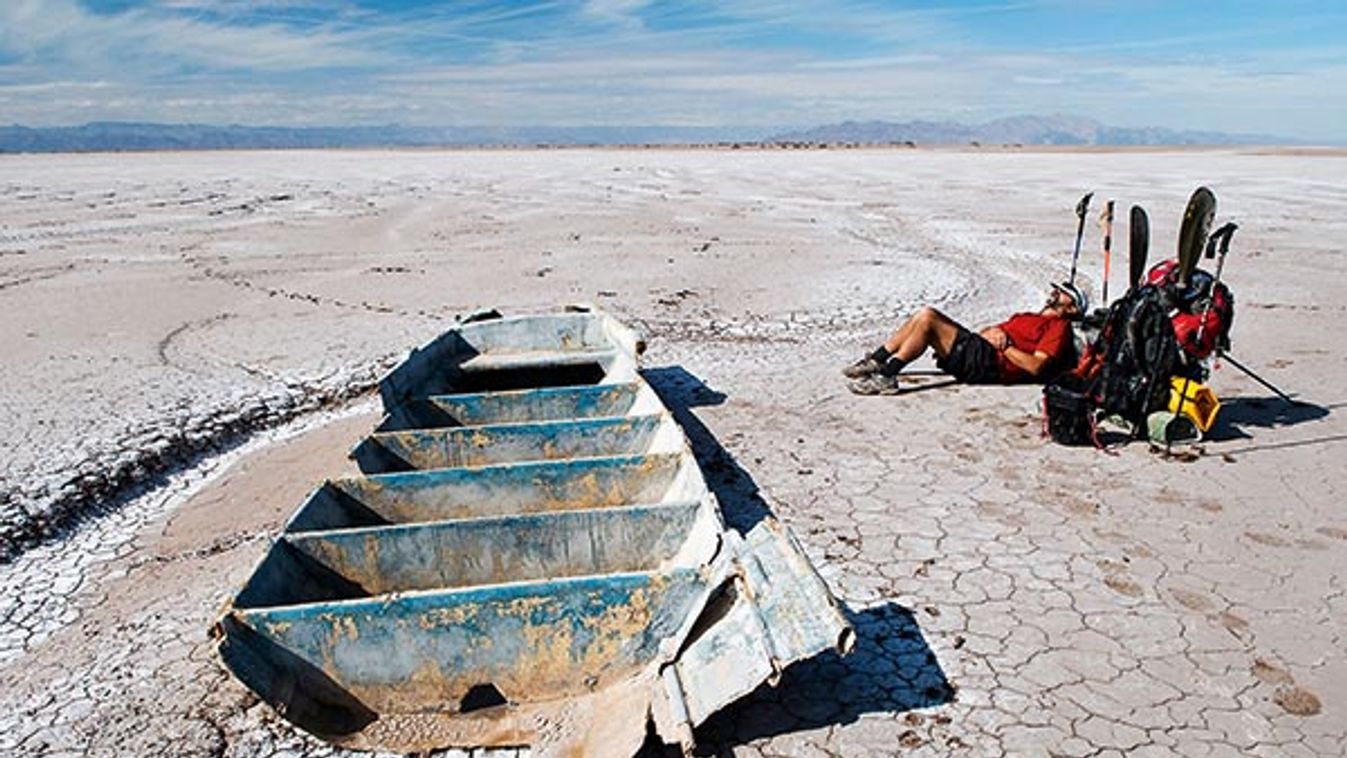 A man rests by an old fishing boat in the dry Colorado River delta.