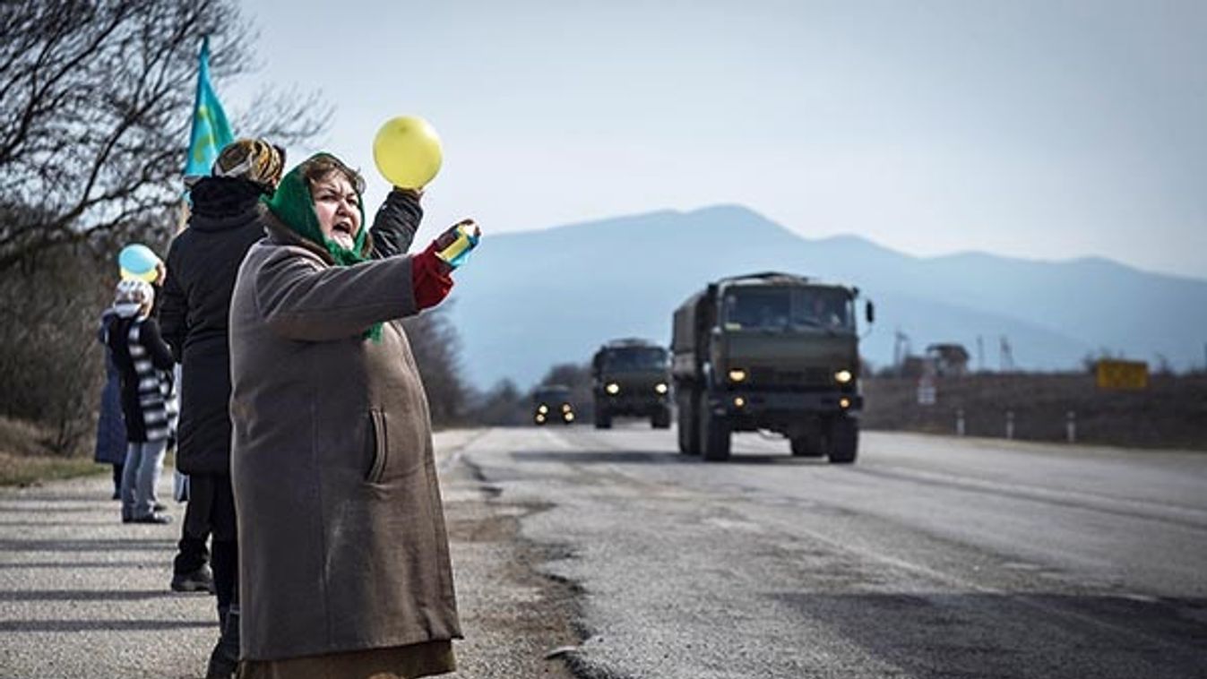 Ethnic Tatar women hold balloons in Ukrainian colors in protest as an unmarked military convoy rides through the village of Kok-asan, in the Crimean r