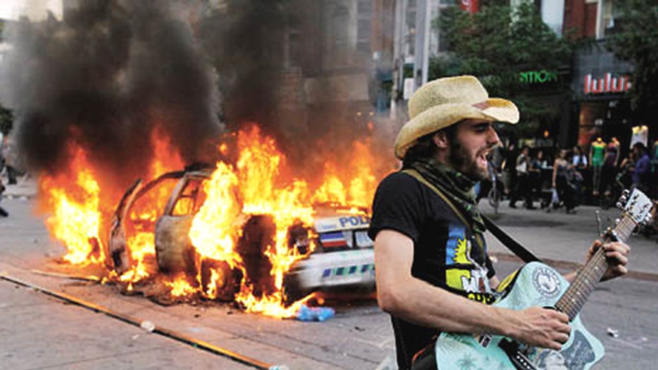 A man plays a guitar in front of a burning police car during a protest against the G20 summit in downtown