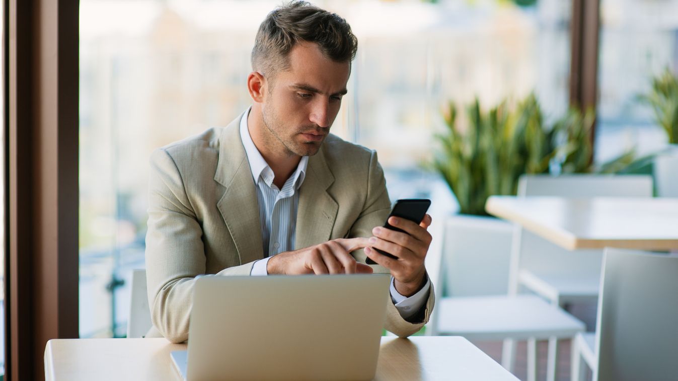 Elegant Businessman working on stock market on mobile phone app and laptop at a cafe