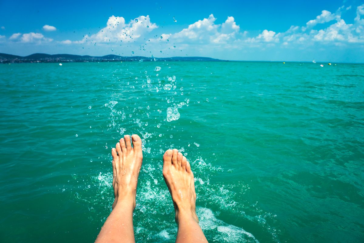 A happy girl woman is kicking feet on a sea lake and splashing water on a sail boat summertime