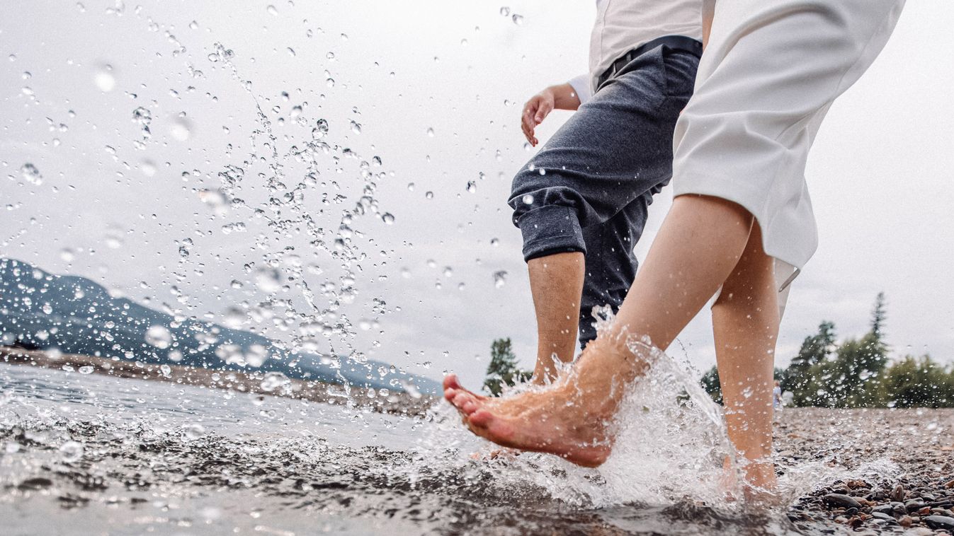 Feet,Exploding,Water.,Legs,At,Shore.,Two,People,Walking,With