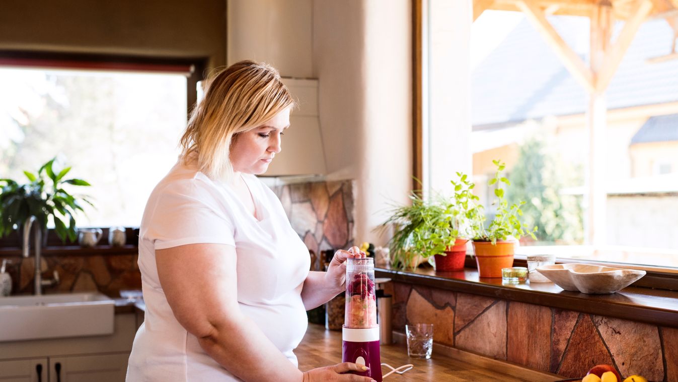 Overweight,Woman,In,The,Kitchen,,Making,Fresh,Smoothie,In,Blender.