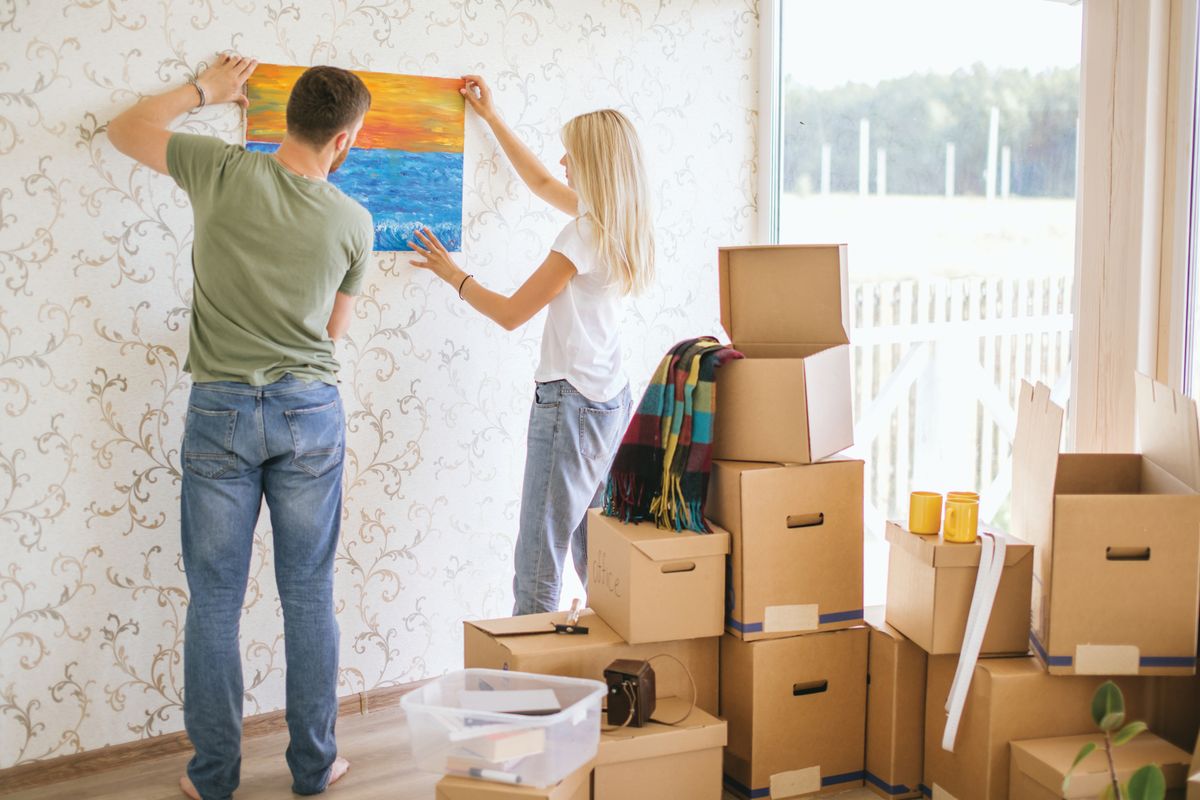 Moving,House.,Young,Couple,Hanging,Picture,On,Wall,In,New