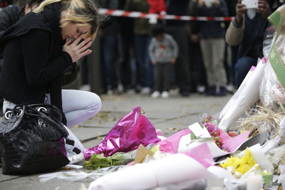 Terrortámadás után - fiatal nő imádkozik a Bataclan közelében felállított kordon mellett felhalmozott virágok előtt a támadás másnapján